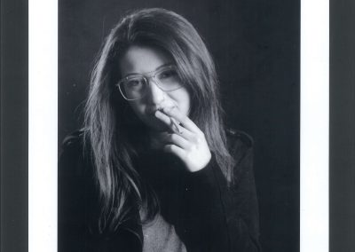 Ritratto b/n di ragazza con gli occhiali e dai capelli lunghi castani mentre fuma una sigaretta.