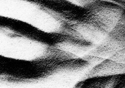 Foto in bianco e nero di segni lasciati sulla sabbia da una mano che creano un paesaggio lunare.